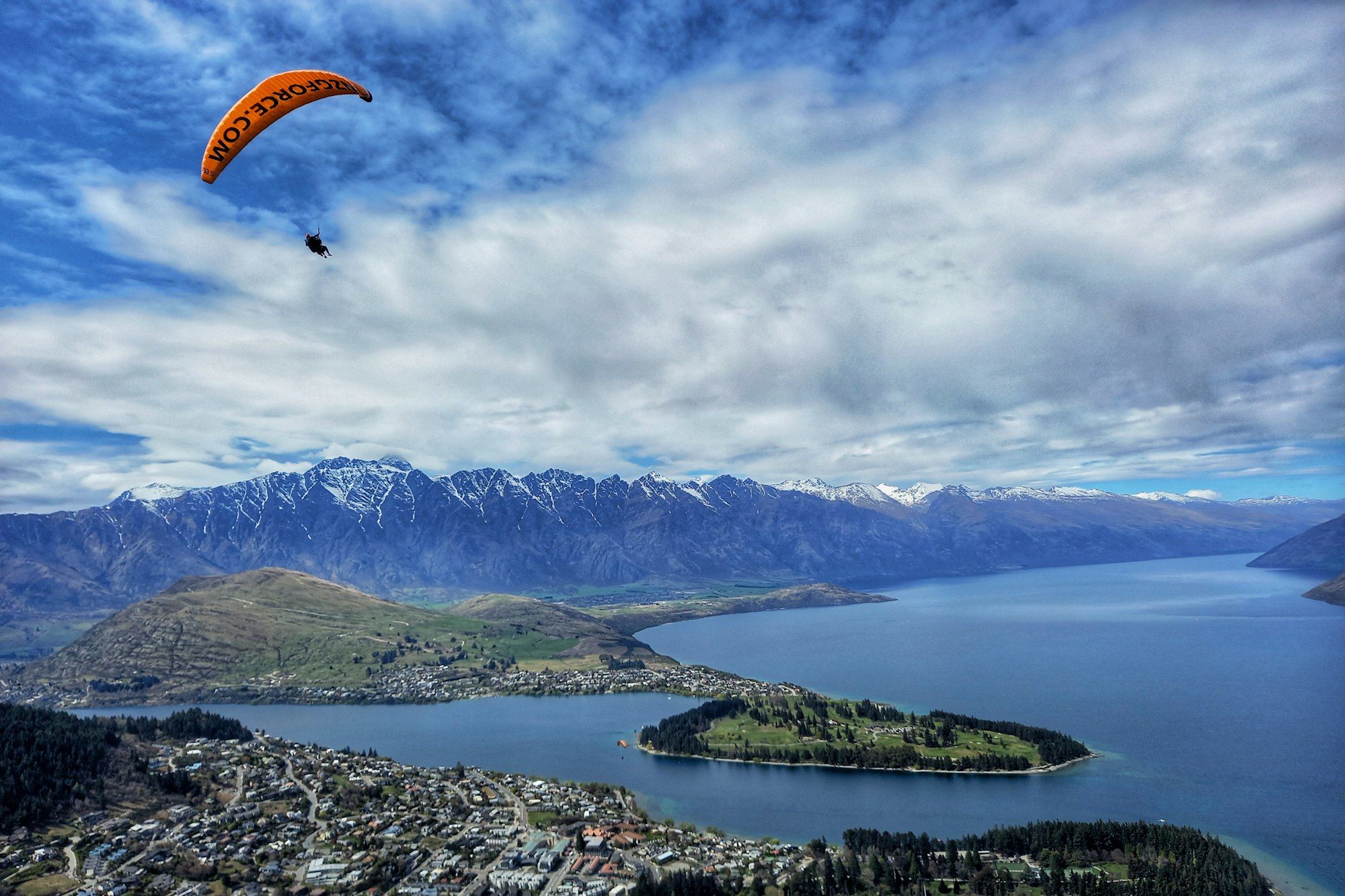 A paraglider flying above Queenstown and the lake, a busy adventure-tourism scene