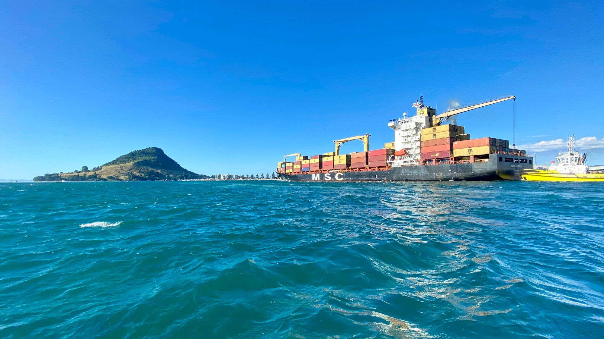 A red cargo ship heading out of the harbour at Tauranga